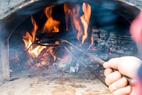 A man holds a waffle iron in a flaming stone oven at Half Crown Bake House in Charleston, South Carolina