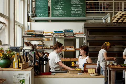 Two workers have a conversation behind the counter at Lille Bakery in Copenhagen, Denmark