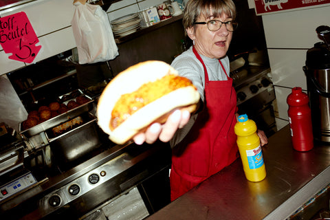 A worker at Fleischerei Domke in Berlin holding out a breakfast sandwich, by Sam A. Harris