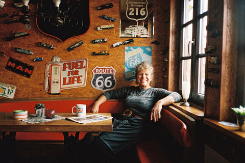 A portrait of Carola Roßberg, owner of Rolly's Trucker imbiss in Berlin, sitting in an American diner style booth by Sam A. Harris, from Fare's magazine, Gut Geist: The Berlin Issue